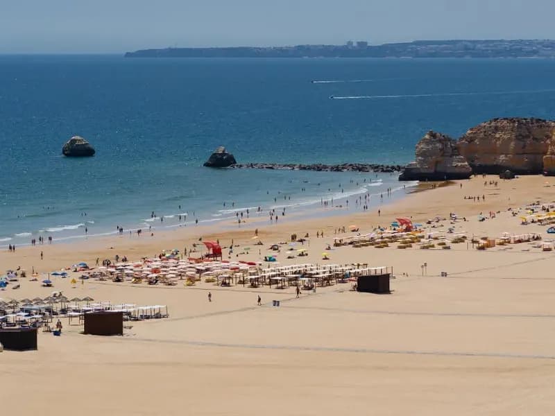 Het brede zandstrand van Praia da Rocha met parasols en rotsformaties in zee, gezien vanaf de kliffen