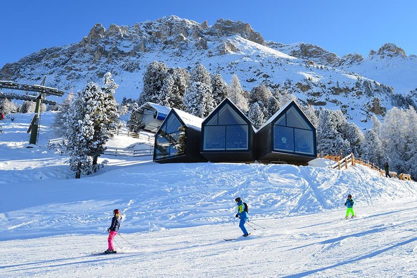 Skiërs op de piste van Obereggen met een modern berghotel en de Dolomieten op de achtergrond
