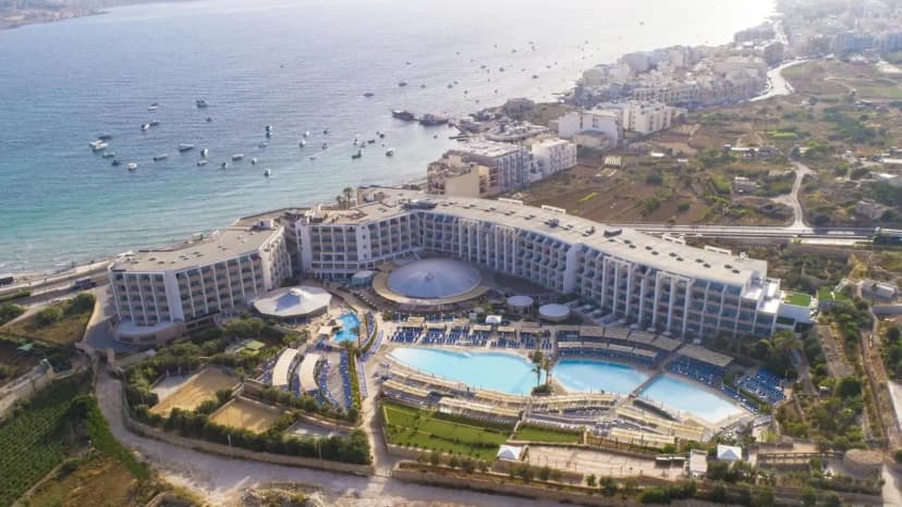 Luchtfoto van een hotelresort aan Mellieħa Bay, met de baai en het dorp Mellieħa op de achtergrond
