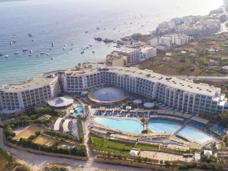Luchtfoto van een hotelresort aan Mellieħa Bay, met de baai en het dorp Mellieħa op de achtergrond