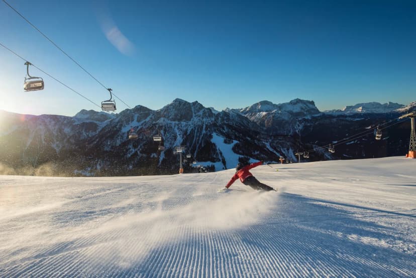 Skiër op een piste in Zuid-Tirol met zicht op kabelliften en de bergtoppen van de Dolomieten