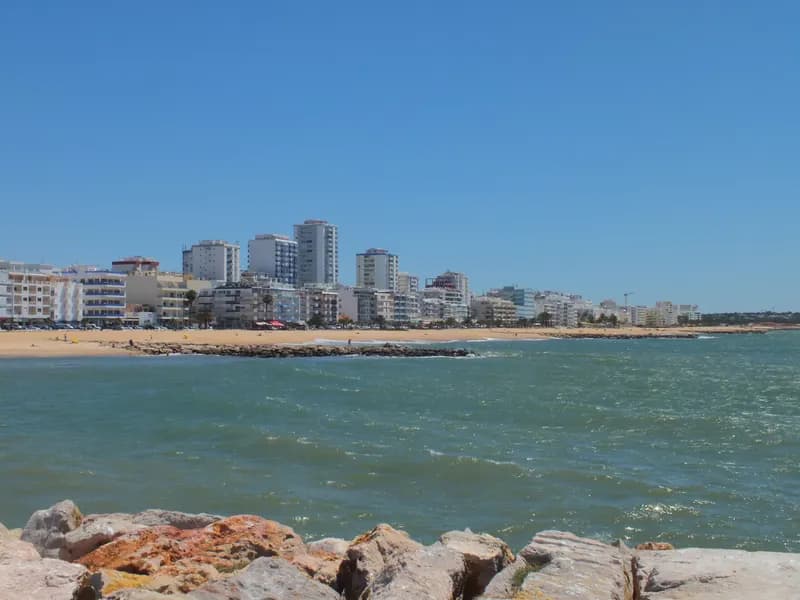 Strand van Quarteira met de zee op de voorgrond en de appartementsgebouwen van de badplaats op de achtergrond