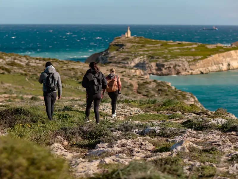 Wandelen op Malta langs de kliffen, drie wandelaars op een kustpad met uitzicht op een baai