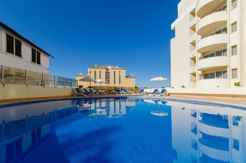 Buitenzwembad met blauwe ligbedden naast het witte appartementsgebouw van Turim Algarve Mor in Praia da Rocha