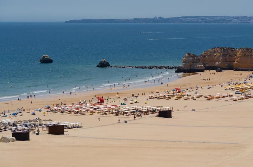 Het brede zandstrand van Praia da Rocha met parasols en rotsformaties in zee, gezien vanaf de kliffen