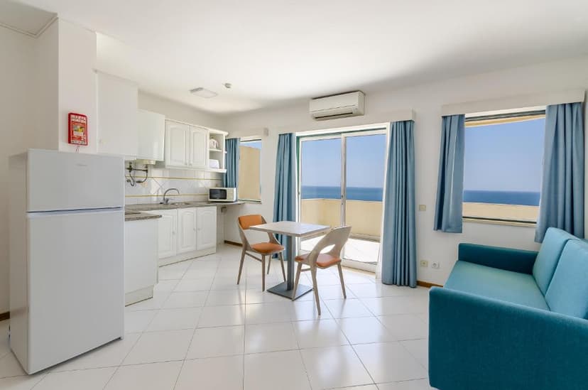 Lichte woonkamer met open kitchenette, eettafel en schuifraam met zicht op zee in een appartement van Turim Algarve Mor