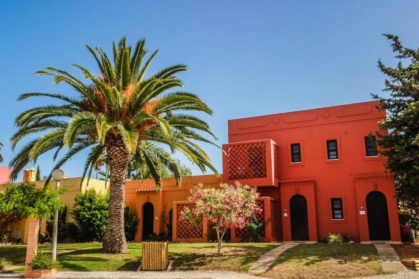 Oranjerood vakantiehuisje met een grote palmboom in de tuin van aparthotel Colina Village in Carvoeiro