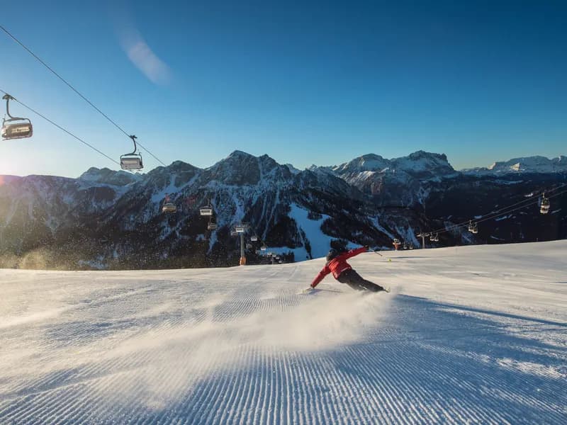 Skiër op een piste in Zuid-Tirol met zicht op kabelliften en de bergtoppen van de Dolomieten