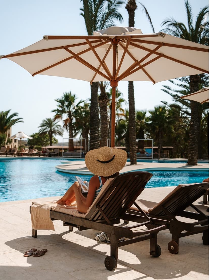 Ligstoelen onder een parasol aan het zwembad tussen palmbomen in een resort op Gozo