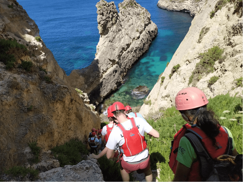 Avonturiers met helm en reddingsvest dalen af langs de rotsen naar de zee tijdens coasteering op Malta