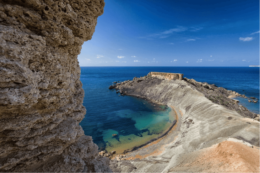 Uitzicht door een rotsboog op een baai met wachttoren aan de Maltese kust