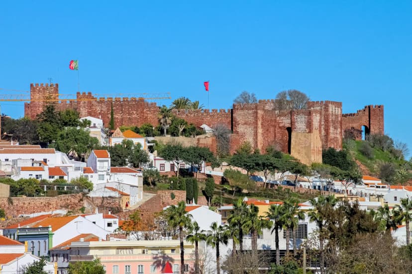 Roodbruine stadsmuren en torens van het kasteel van Silves boven de witte huizen en palmbomen van de stad