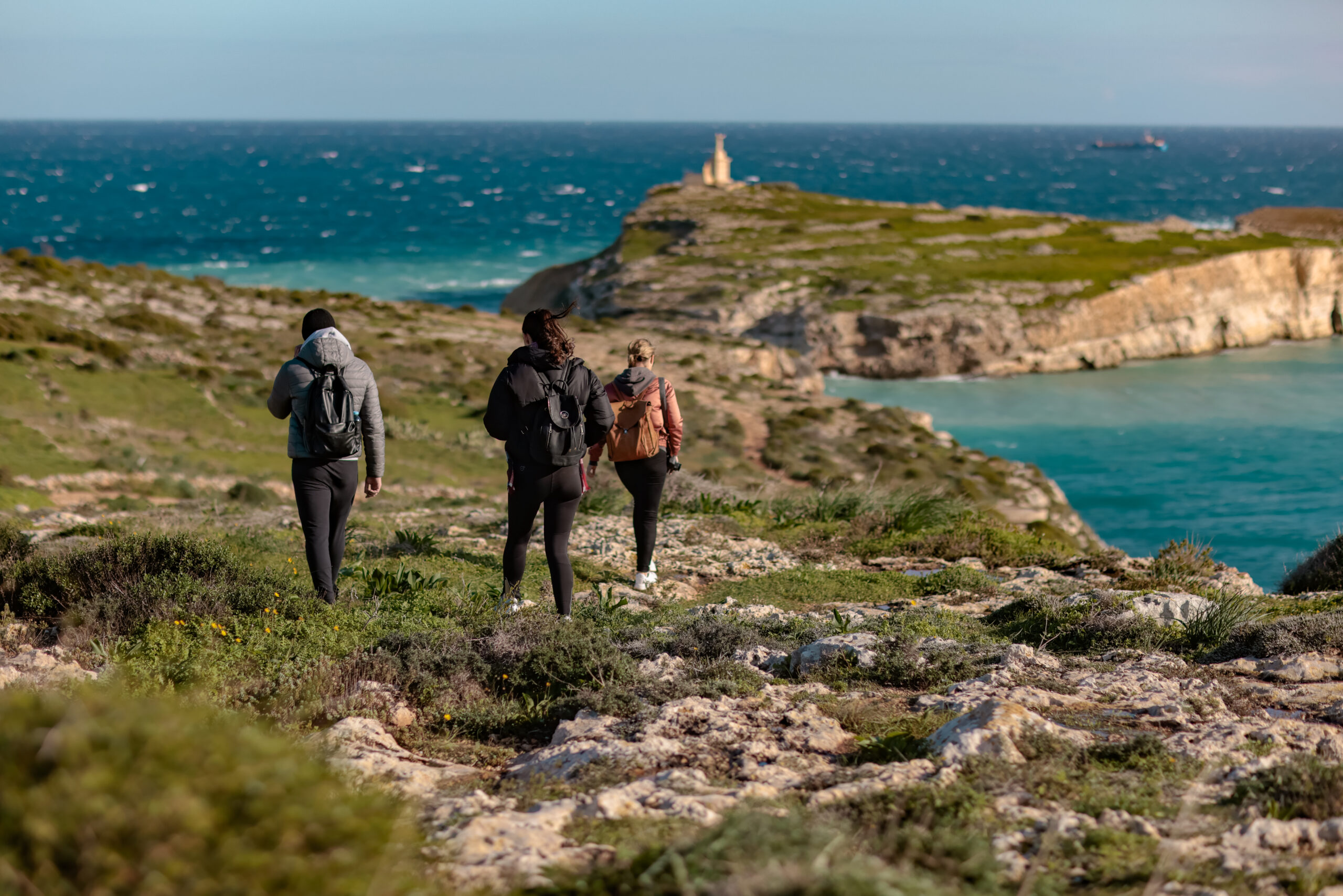 Wandelen op Malta langs de kliffen, drie wandelaars op een kustpad met uitzicht op een baai